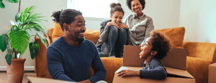 Quatro familiares reunidos na sala sorrindo e criança sorridente
  dentro da caixa de papelão.