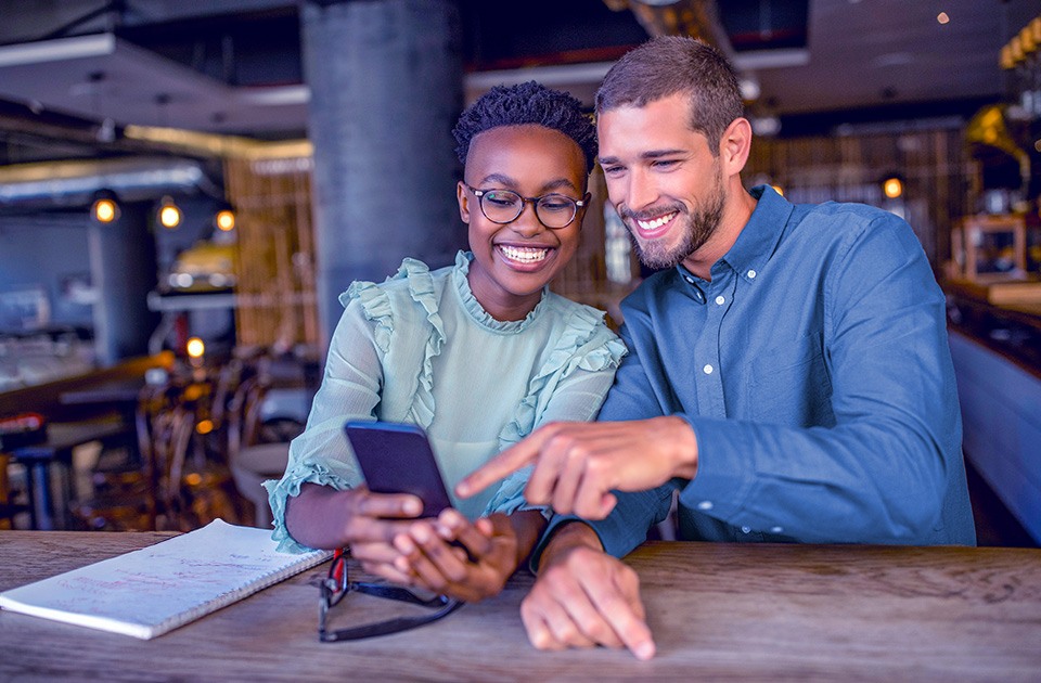 Casal sorridente olhando para um celular juntos.