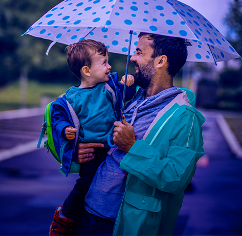 Pai segurando um guarda-chuva e sorrindo para o filho pequeno.